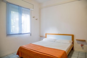 A single bed with a wooden headboard in a room with a window and a small shelf. - Comfy Accommodation With Balcony (Eraclea)