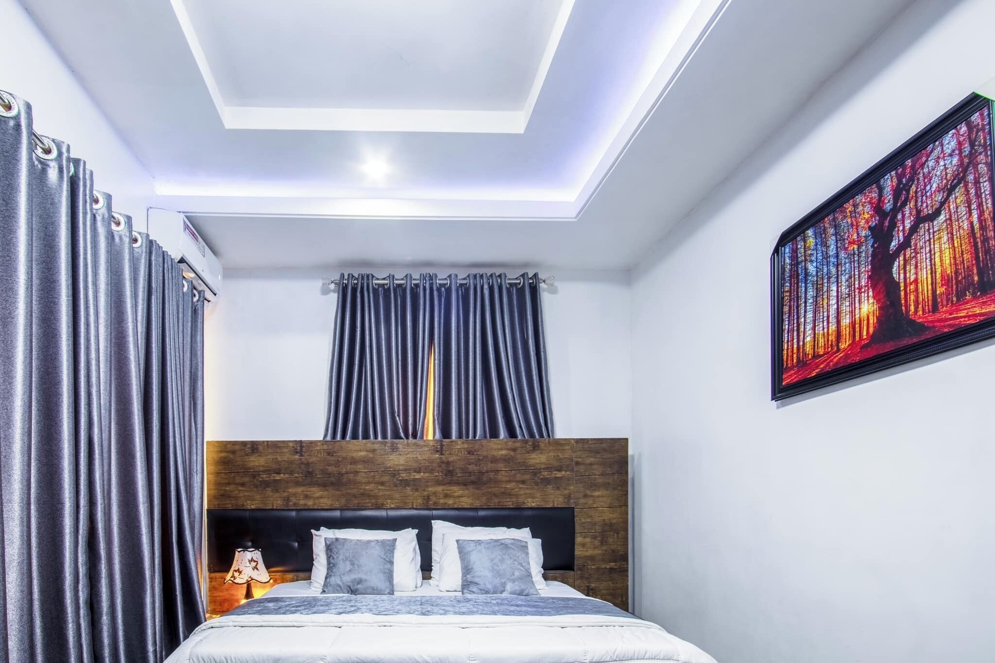 Una camera da letto moderna con una testiera in legno, un letto grande con biancheria grigia, una lampada a soffitto e un quadro appeso al muro.