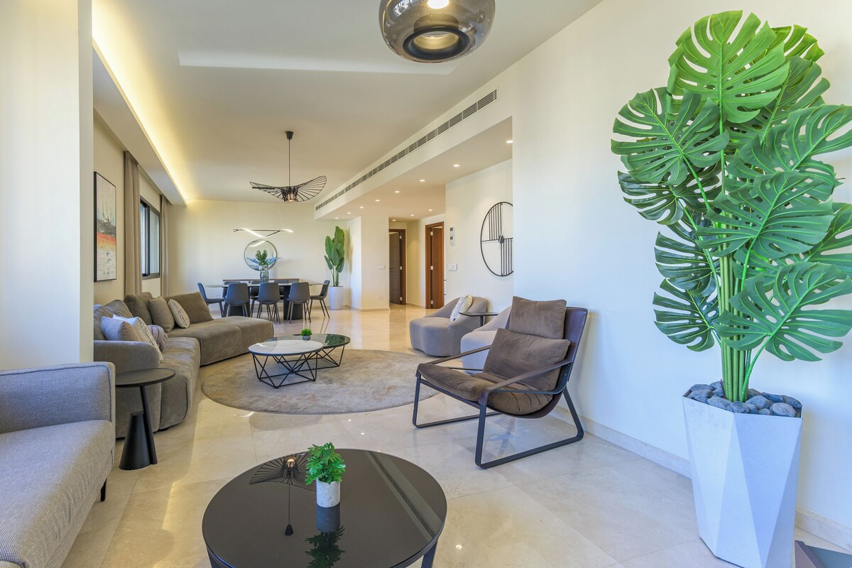 Un salon moderne avec un canapé d’angle, une table basse et une grande plante en pot.