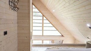 Ein Schlafzimmer mit schrägverdeckter Decke, Holzwänden und einem großen Fenster, darin ein Bett.