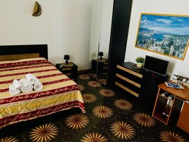Una habitación de hotel con una cama, televisión, escritorio y un cuadro de paisaje urbano en la pared.