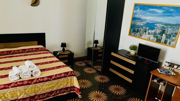 A hotel room with a bed, a TV, a desk, and a cityscape painting on the wall. - Palazzo Armony (Bitritto)