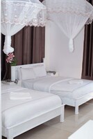 Habitación de hotel con dos camas, una cama con dosel blanco, una mesita de noche y una pequeña mesa con lámpara.