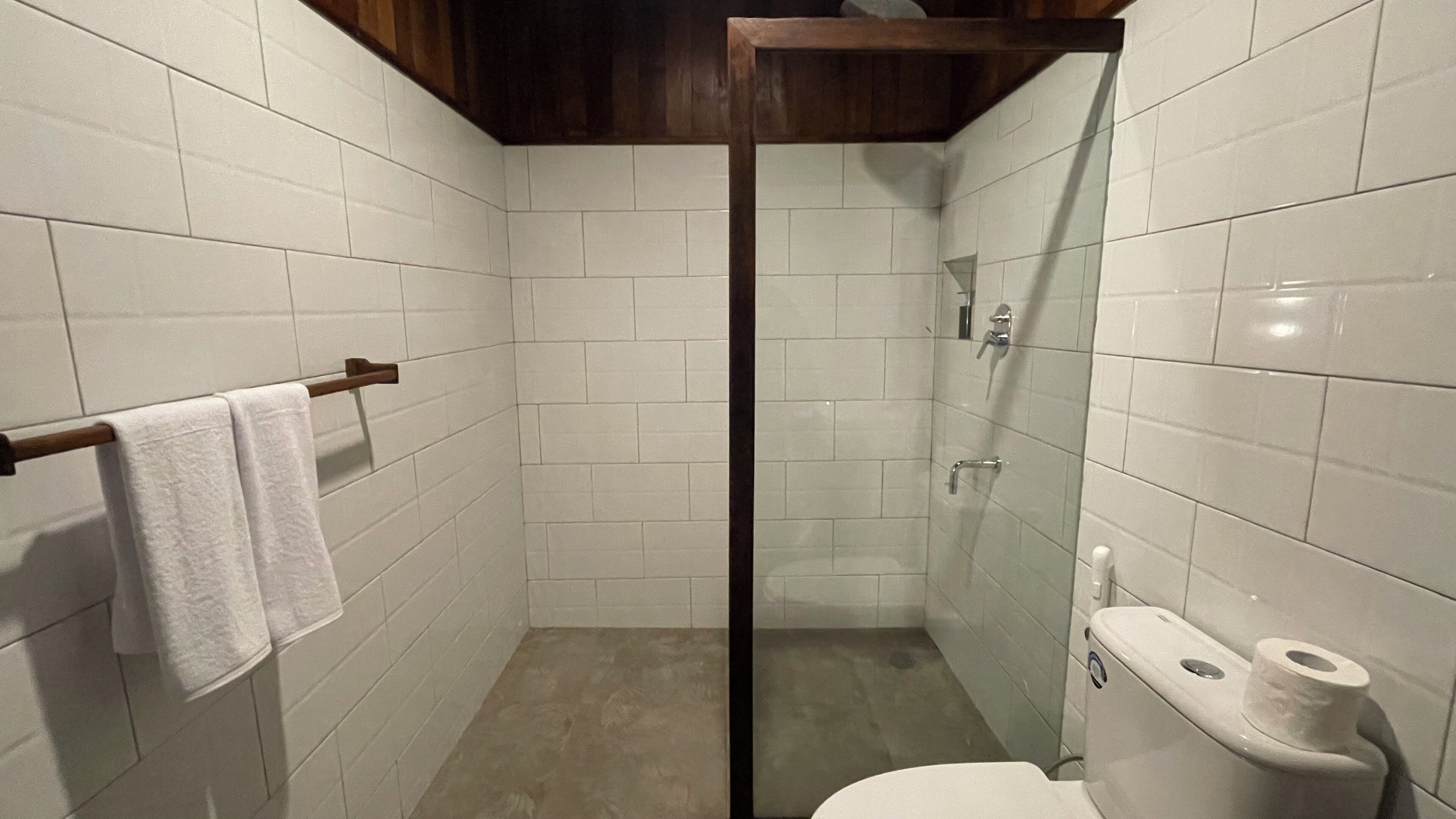 Un box de ducha pequeño y cerrado, con azulejos blancos, una puerta de cristal y techo de madera.