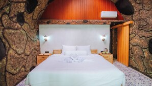 A bed with white linens and a towel art arrangement, wooden headboard, two bedside tables, and a stone wall backdrop. - The Jungle Pots (Payangan)