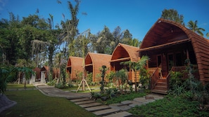 A row of wooden cabins with curved roofs, surrounded by lush greenery and a clear blue sky. - The Jungle Pots (Payangan)