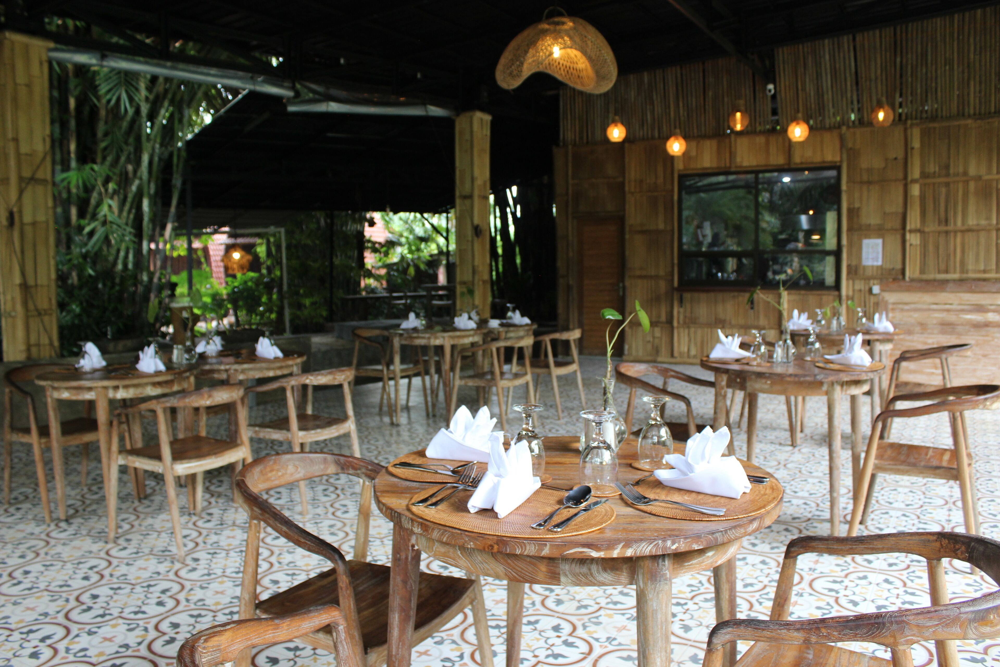 A restaurant with round wooden tables set with white napkins, cutlery, and glassware.