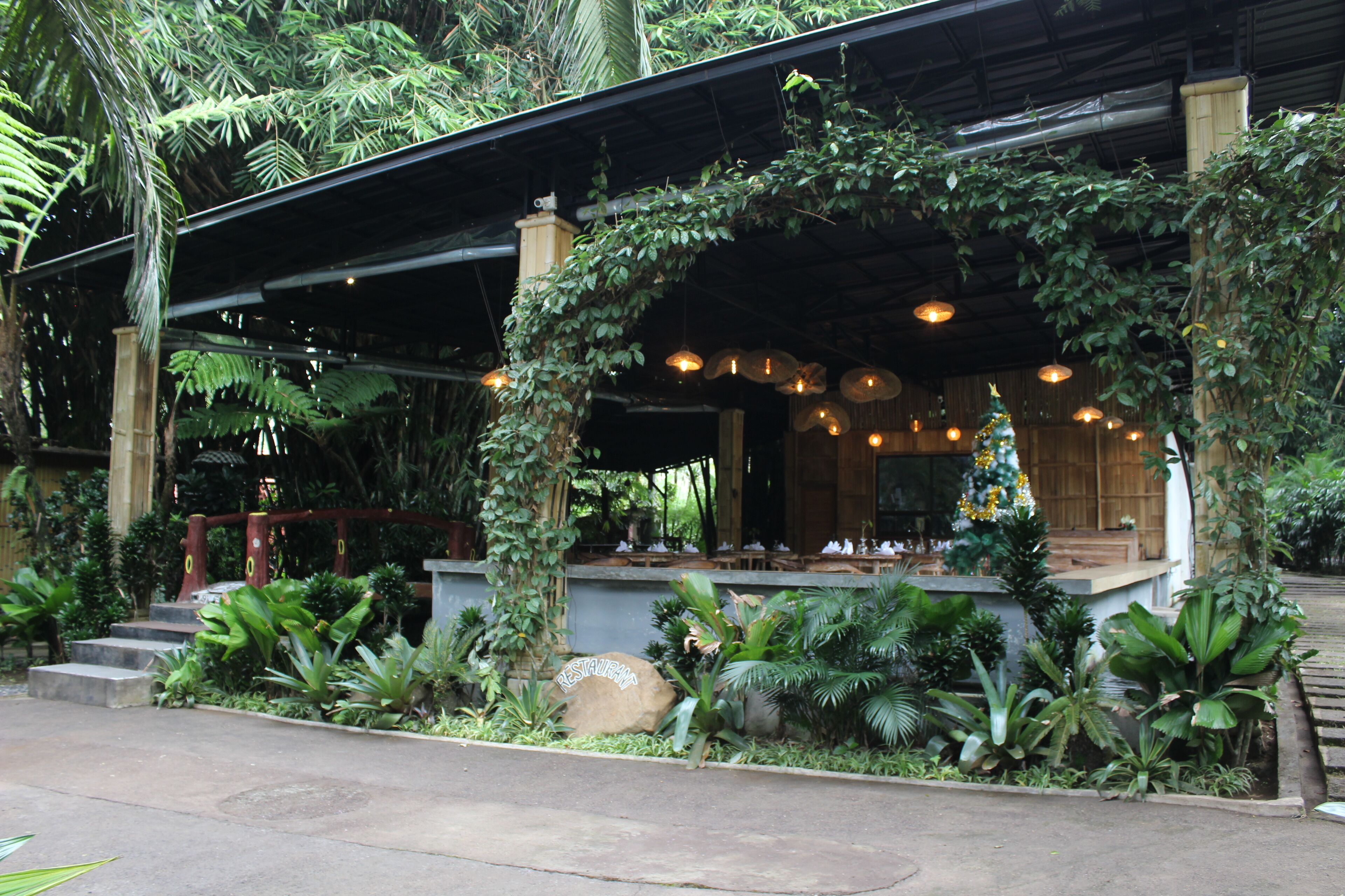A restaurant with a covered outdoor seating area, surrounded by lush greenery and plants.