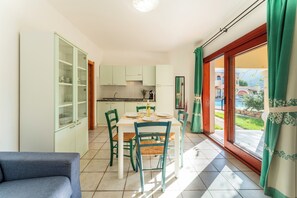 A dining area with a table and chairs, a kitchen in the background, and a view through a glass door. - Cozy Accommodation in Beautiful Sardinia (Badesi)