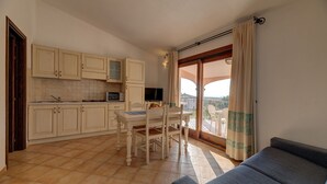 Et kompakt køkken med spiseplads, en sofa og en balkon med gardiner.