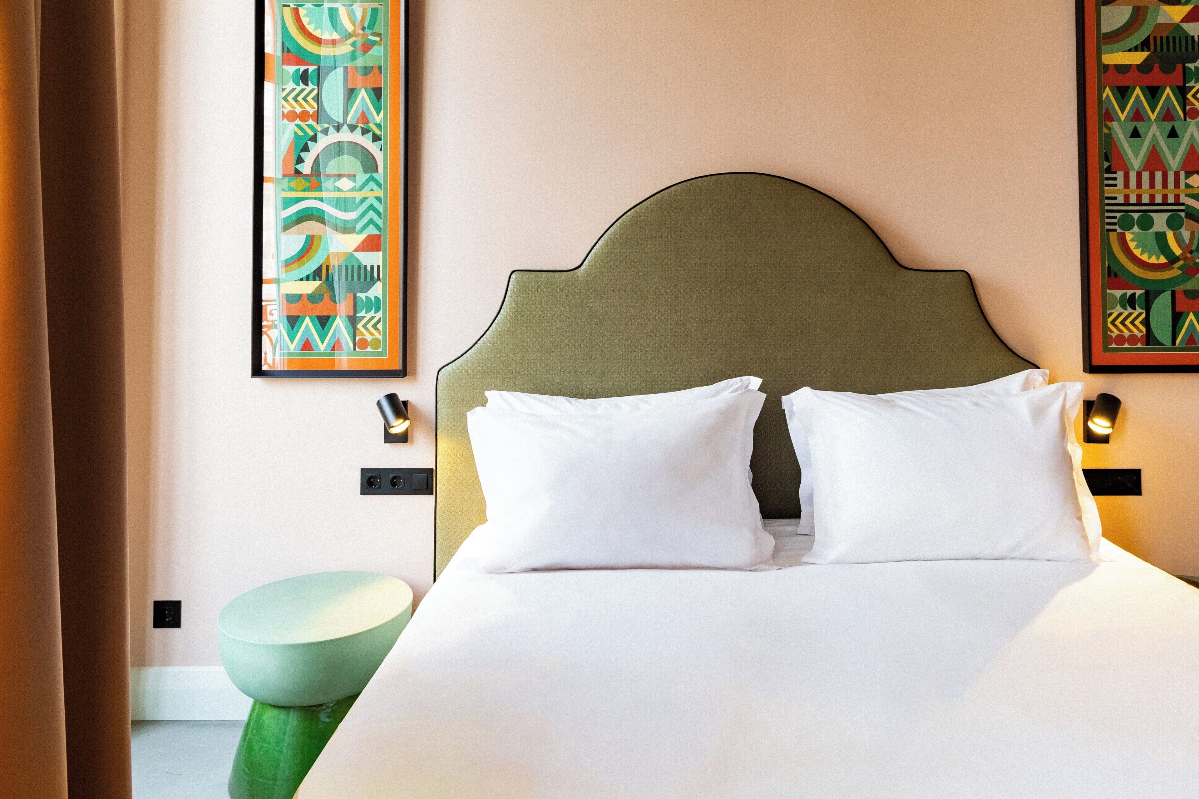 Een hotelkamer met een bed, een groene kruk en twee wandlampen.