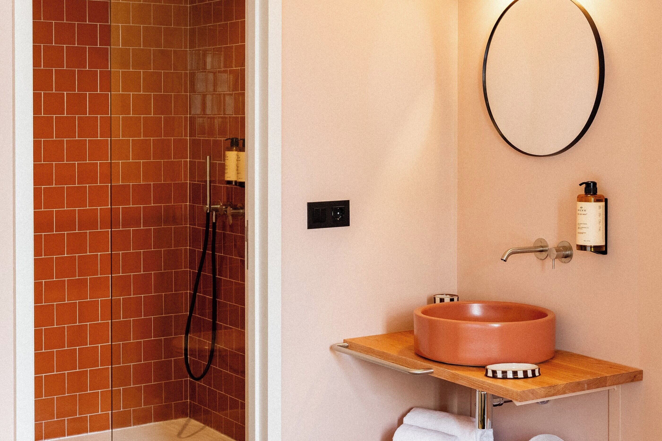 A bathroom with a shower, a sink with a round basin, a mirror, and a towel rack.