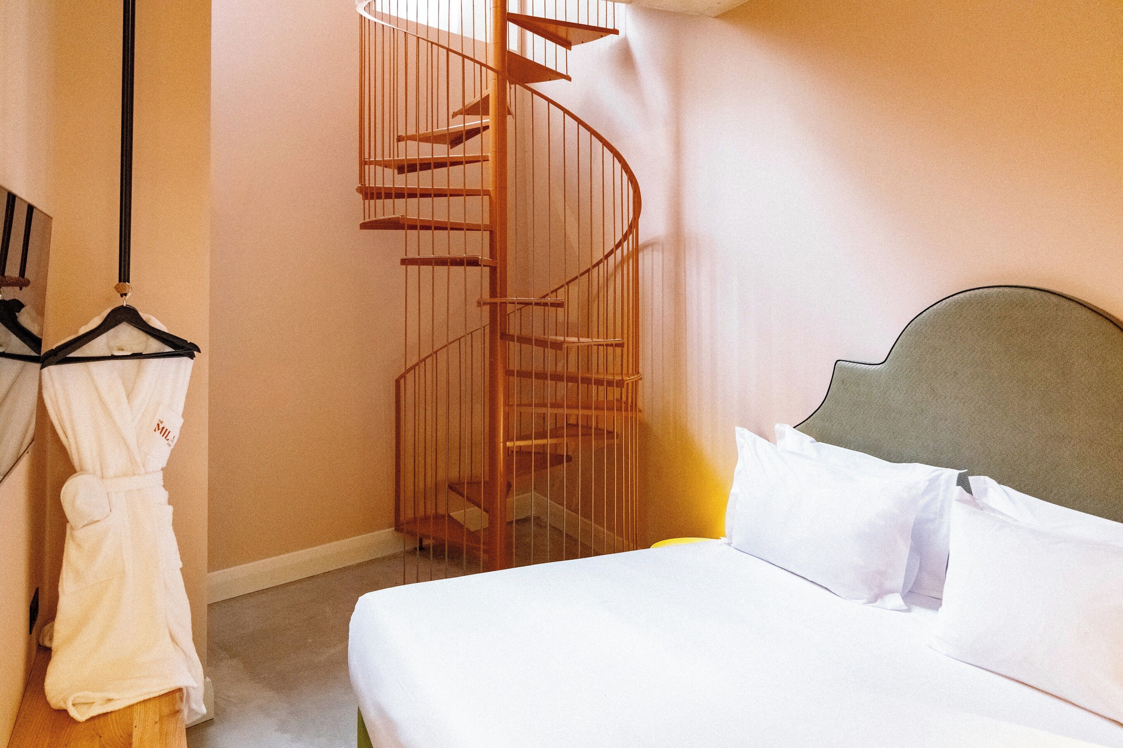 A bedroom with a bed, a wooden spiral staircase, and a robe hanging on a rack.