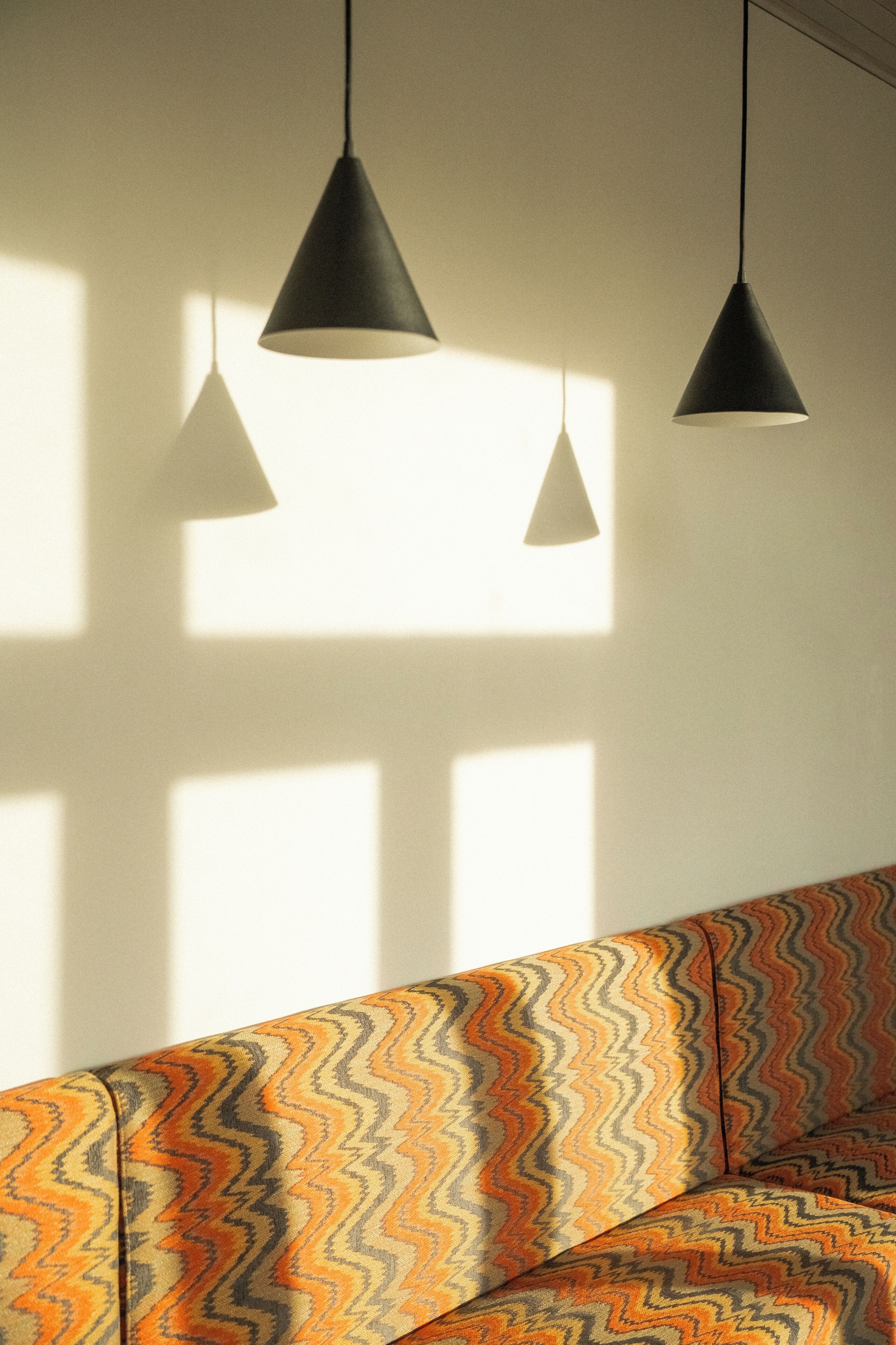 Quarto com sofá estampado, duas luminárias pendentes e uma janela projetando sombras na parede.