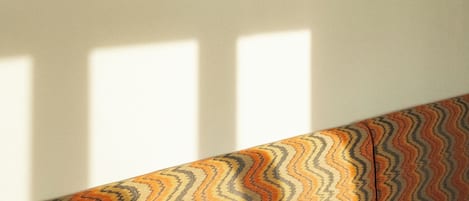 A room with a patterned sofa, two pendant lights, and a window casting shadows on the wall.