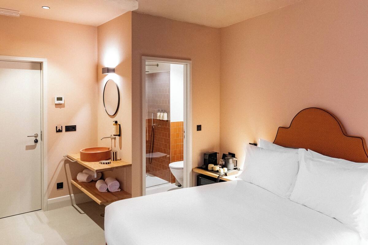 A hotel room with a bed, a bathroom with a sink, and a shower.