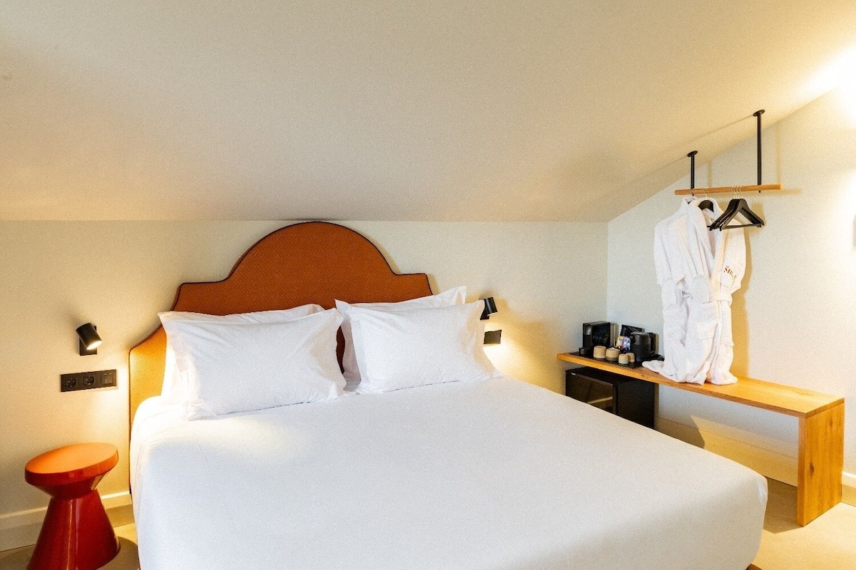 A hotel room with a bed, bedside table, nightstand, and a robe hanging on a rack.