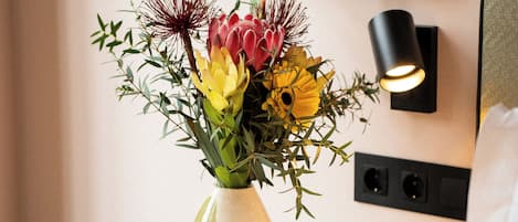 A vase with flowers on a bedside table, a framed picture on the wall, and a lamp beside the bed.