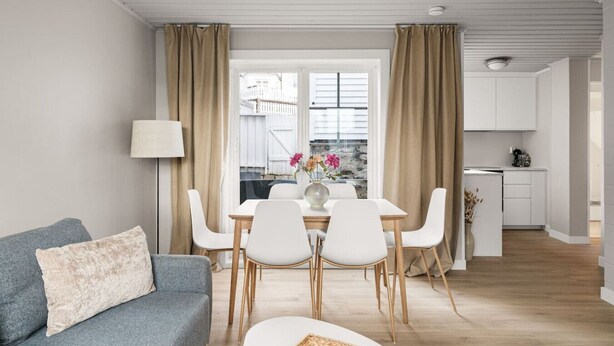 A modern living room with a grey sofa, a dining table with white chairs, and a kitchen area in the background. - The Heart of Bergen - Central & Stylish (Bergen)