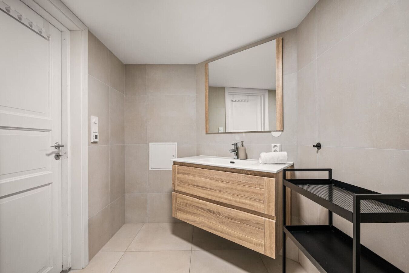 Un baño moderno con tocador de madera, un espejo grande y un estante de metal negro.