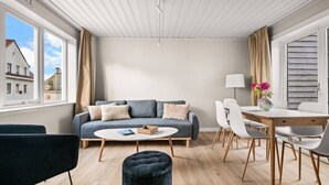 A modern living room with a sofa, round coffee table, ottoman, and dining area with chairs and a table. - The Heart of Bergen - Central & Stylish (Bergen)