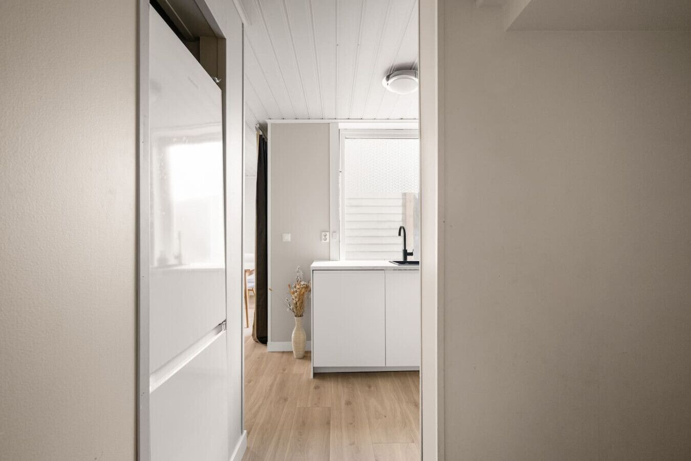 A narrow hallway leading to a kitchen with white cabinets and a window.
