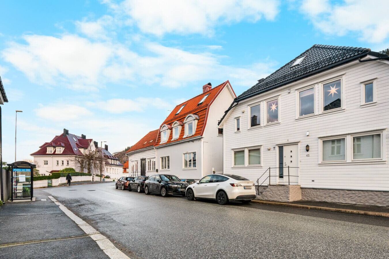 Una calle con edificios residenciales, coches aparcados y una parada de autobús.