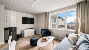 A modern living room with a fireplace, a sofa, a TV, and a view of a cityscape through large windows. - The Heart of Bergen - Central & Stylish (Bergen)