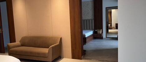 Ein modernes Hotelzimmer mit einem beigen Sofa, einem Bett und einem großen Fenster.
