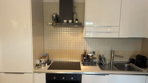 Uma cozinha moderna com armários brancos, fogão preto, pia e bancada com diversos objetos.