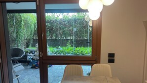 Uma sala de jantar moderna com uma mesa grande e cadeiras, um lustre pendurado e vista para um jardim através de portas de vidro.