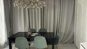 Uma sala de jantar com mesa preta, cadeiras verdes com pés dourados e um lustre.