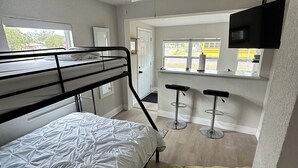 Un lit superposé avec un matelas blanc, un ventilateur de plafond, un canapé vert et un téléviseur fixé au mur.