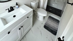 Une salle de bain avec un lavabo, des toilettes et une douche, le tout de couleur blanche.