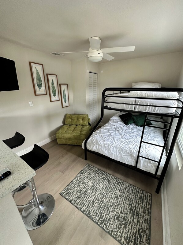 A compact room with a bunk bed, a desk with a chair, a ceiling fan, and framed leaf artwork on the wall.