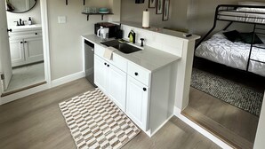 Une chambre à coucher compacte et moderne, équipée d’un lit superposé, d’une petite kitchenette et d’une salle de bain visible à travers une porte ouverte.