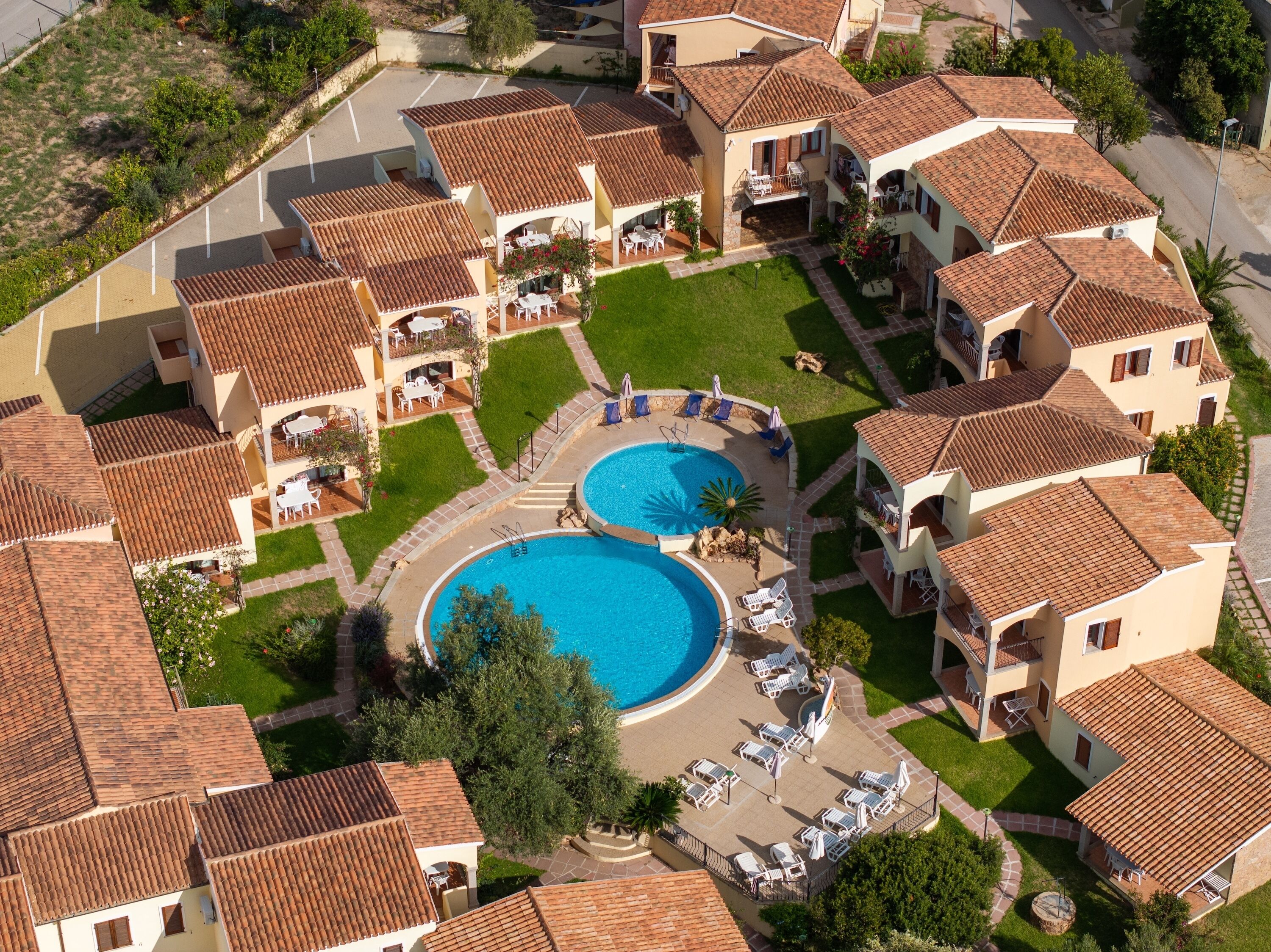 A residential complex with two swimming pools, outdoor seating areas, and a well-maintained lawn.