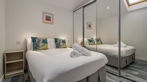 Moderni hotellihuone, jossa on suuri sänky, vaatekaappi ja pieni yöpöytä.