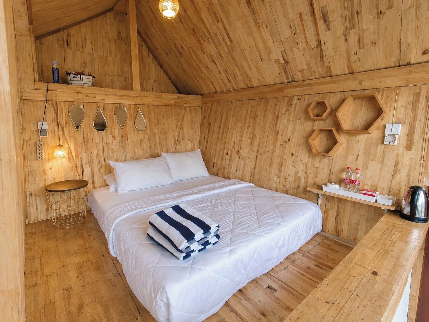 A wooden room with a bed, a small table, and a shelf with items.