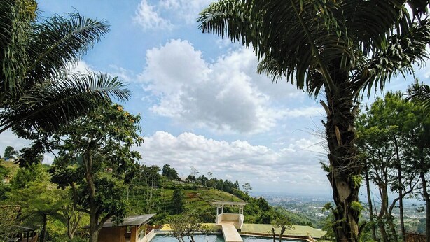 A pool area with a view of a cityscape, surrounded by lush greenery and palm trees. - Dulang Resort & Resto (Lembang)