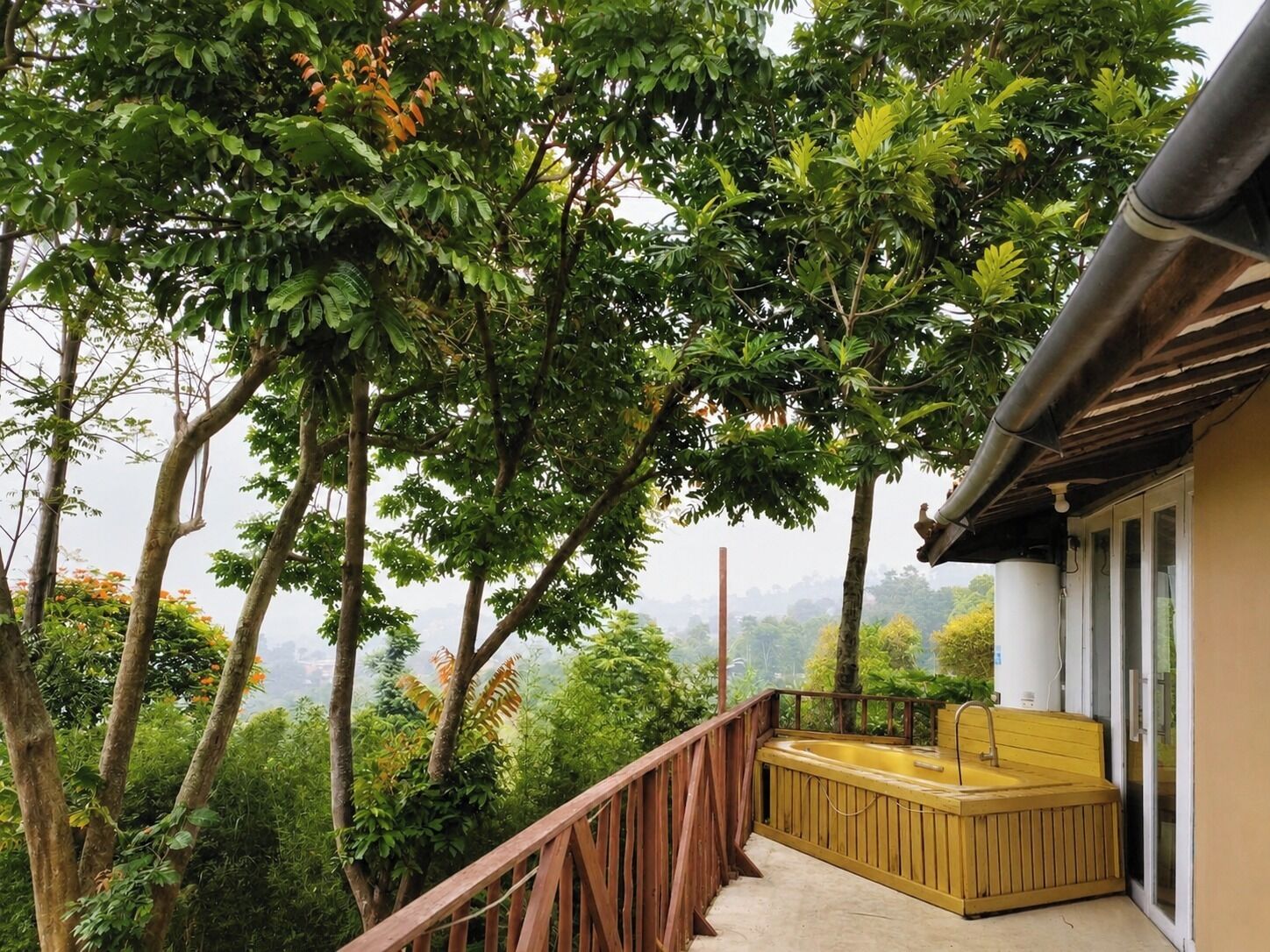 A balcony with a wooden bench and a hot tub, surrounded by lush greenery and trees.