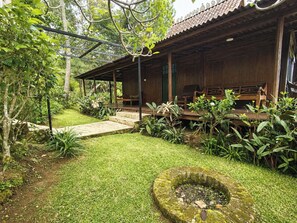 A wooden cabin with a covered porch, stone steps, and lush greenery. - Dulang Resort & Resto (Lembang)