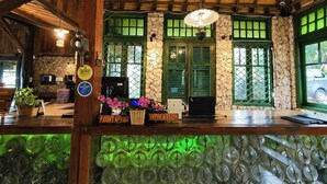 A reception area with a wooden ceiling, stone walls, green-framed windows, a reception desk, and a green-lit glass display. - Dulang Resort & Resto (Lembang)
