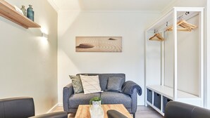 Ett modernt vardagsrum med en grå soffa, ett soffbord i trä och svarta stolar. På väggen finns en hylla med dekorativa föremål och ovanför soffan hänger en tavla.