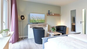 Una habitación de hotel moderna con una cama, un escritorio, una silla, un televisor, una mesita con un jarrón de flores y una planta en maceta.