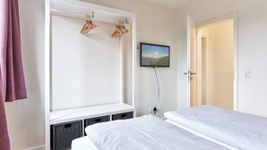 A bedroom with two beds, a wardrobe, a television, and a door leading to another room. - House SeeZeit, Apartment 07 (Timmendorfer Strand)