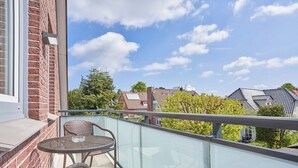 A balcony with wicker furniture and a glass railing, overlooking a residential area with houses and trees. - House SeeZeit, Apartment 07 (Timmendorfer Strand)