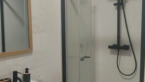 A modern bathroom with a glass-enclosed shower, a white sink with a black faucet, and a wooden vanity. - Le Derroja - Perpignan (Perpignan)