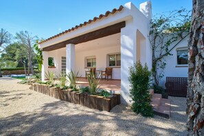 A white building with a covered patio, wooden planters with plants, and a gravel driveway. - Villa in lámetlla de Mar (Sant Jordi d'Alfama)