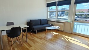 A room with a wooden floor, a sofa, a table with chairs, and a small white table.